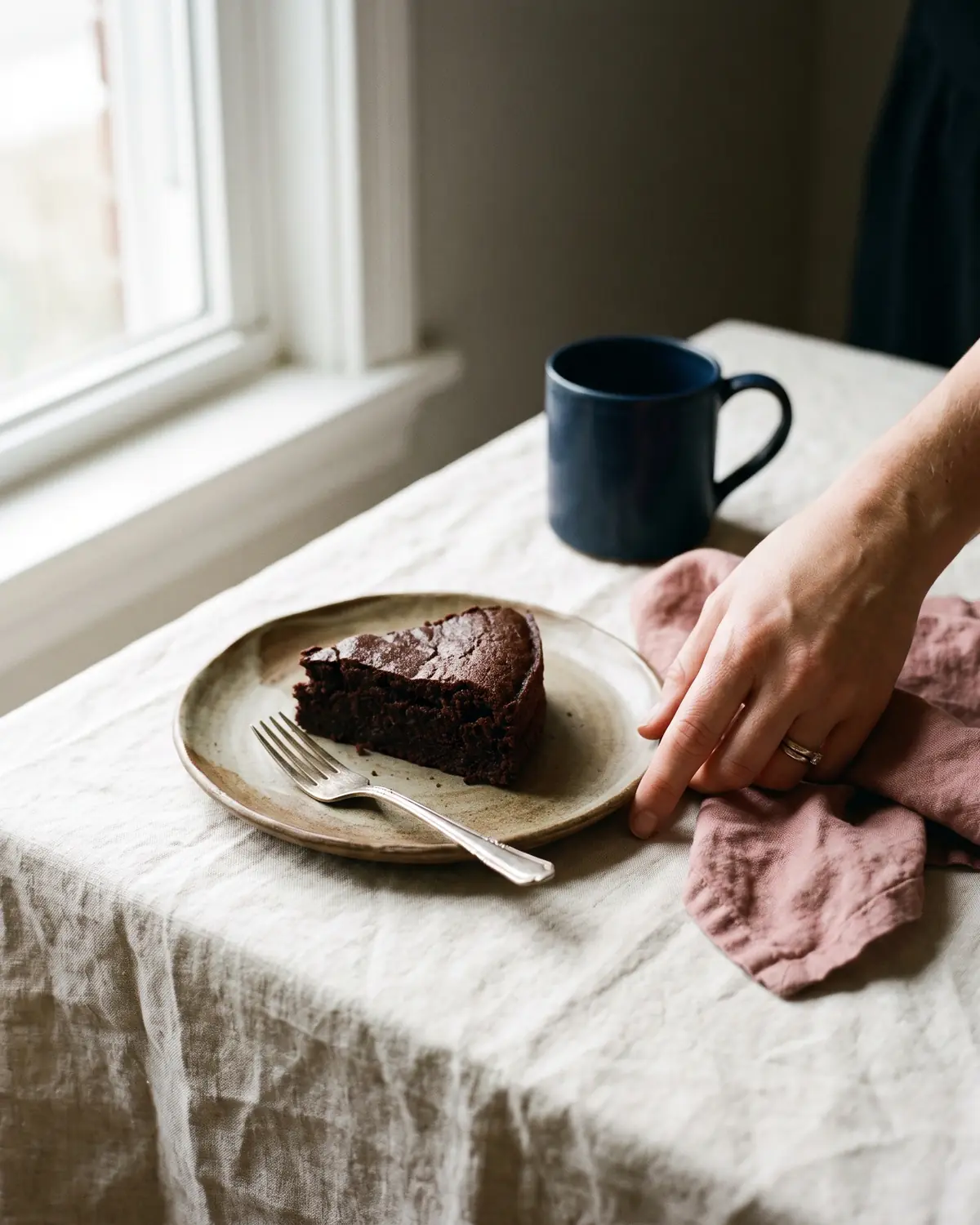 Stuk chocoladetaart op een bord, een hand aarzelt ernaast