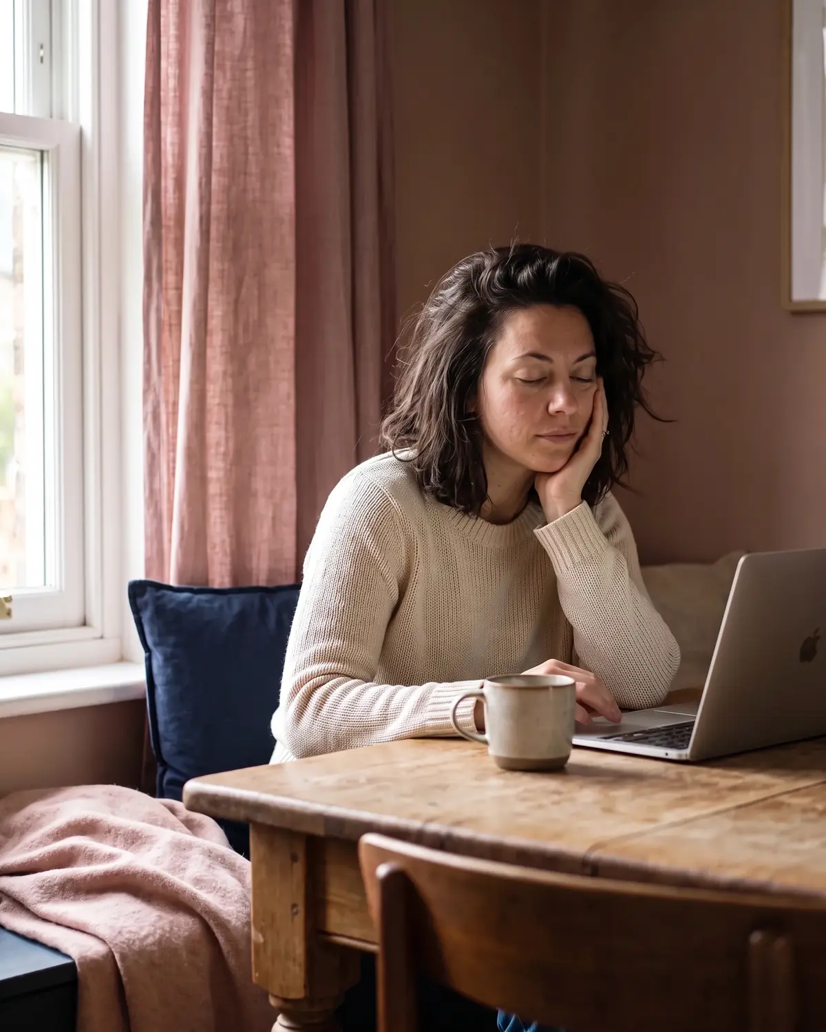 Vermoeide vrouw rust even met gesloten ogen aan de keukentafel